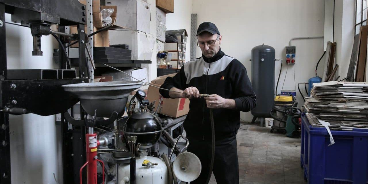 Mantenimiento del aire comprimido en una nave industrial Operario revisando una linea de aire comprimido en un taller, con el deposito del compresor al fondo