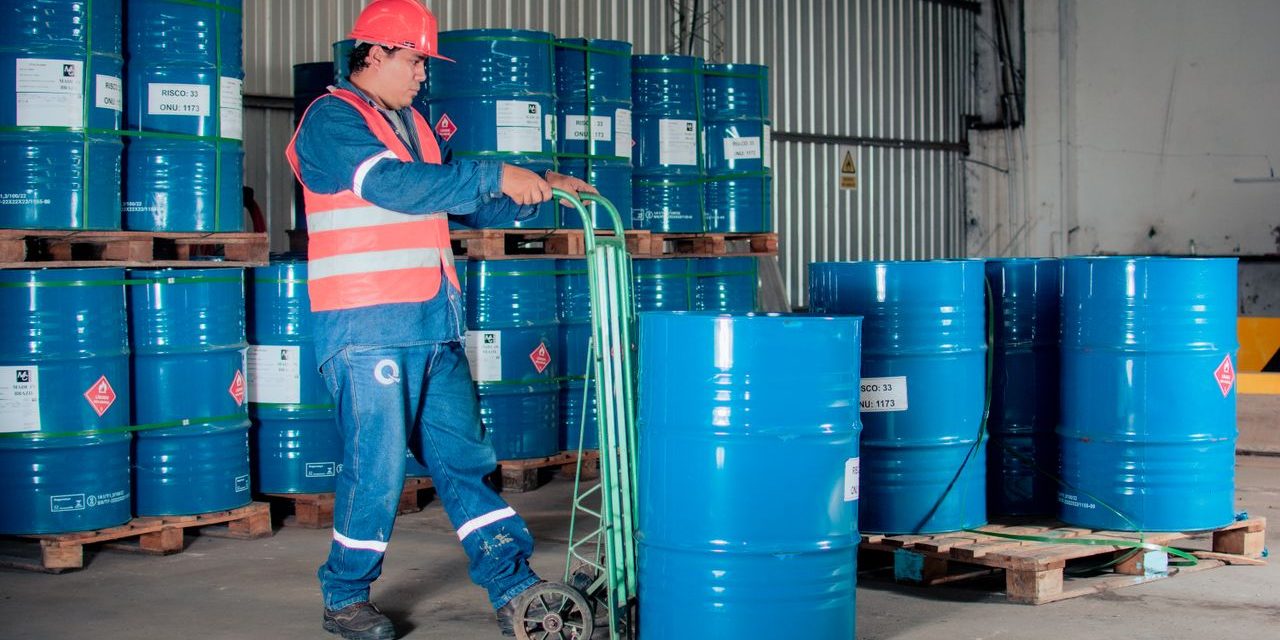 Almacenamiento de productos quimicos e inflamables en una nave industrial Operario con casco y chaleco reflectante trasladando un bidón de producto químico en el almacén de una nave industrial