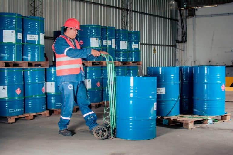 Operario con casco y chaleco reflectante trasladando un bidón de producto químico en el almacén de una nave industrial