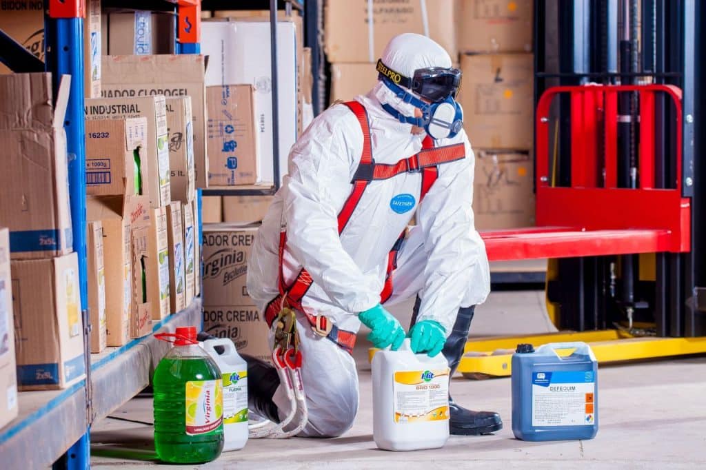 Trabajador con buzo, mascarilla y guantes manipulando envases de producto quimico en un almacen