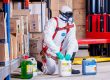 Trabajador con buzo, mascarilla y guantes manipulando envases de producto quimico en un almacen