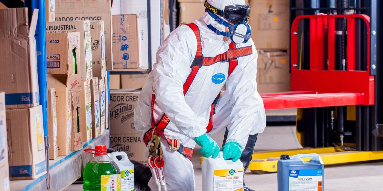 Ficha de datos de seguridad de un producto quimico Trabajador con buzo, mascarilla y guantes manipulando envases de producto quimico en un almacen