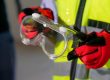 Operario con chaleco reflectante sosteniendo unas gafas de seguridad con guantes de proteccion