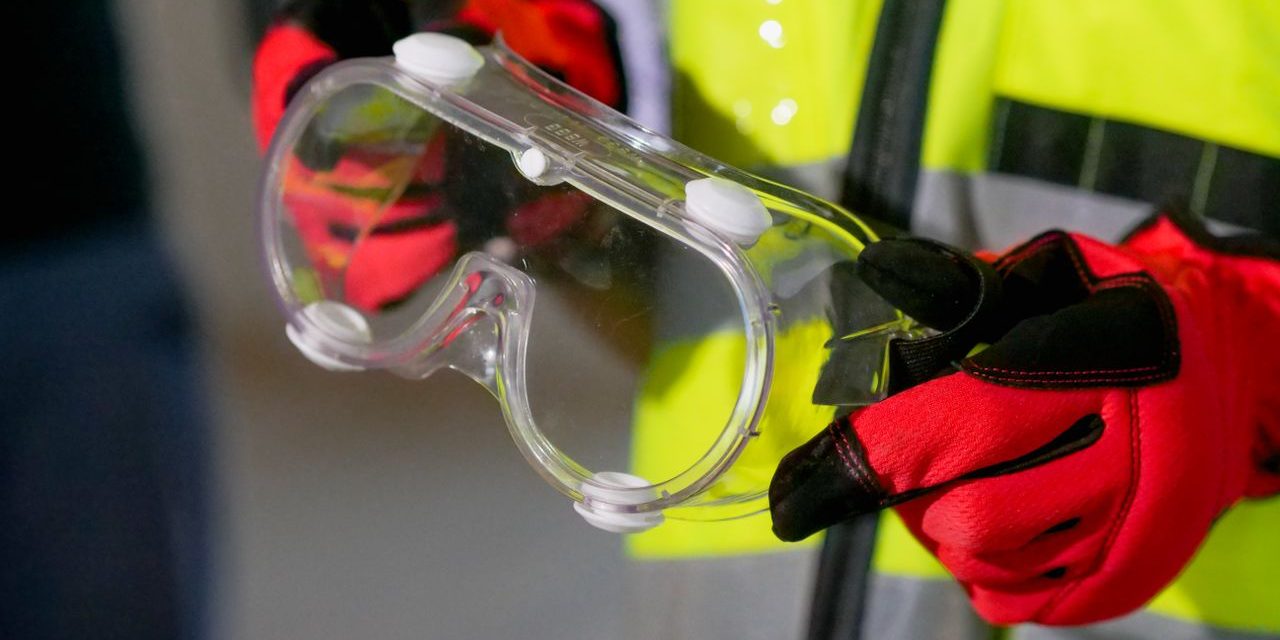 Operario con chaleco reflectante sosteniendo unas gafas de seguridad con guantes de proteccion