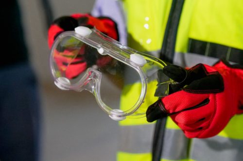 Operario con chaleco reflectante sosteniendo unas gafas de seguridad con guantes de proteccion