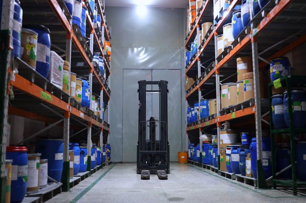 Pasillo de un almacen industrial con estanterias cargadas y una carretilla elevadora al fondo