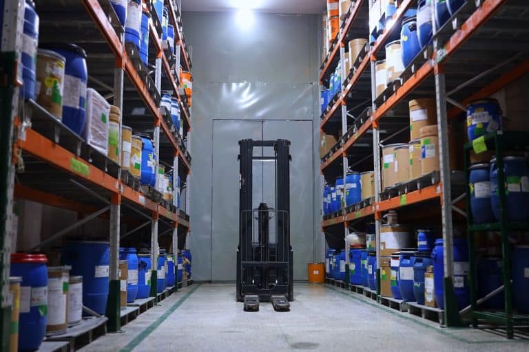 Pasillo de un almacen industrial con estanterias cargadas y una carretilla elevadora al fondo